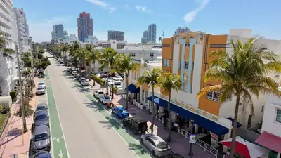 a city street with palm trees and buildings and cars at Art Deco Suite Steps from Beach in South of Fifth in Miami Beach