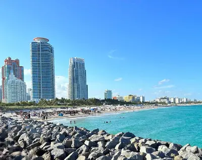 a beach with people in the water and buildings at Art Deco 1 Bedroom Apartment Steps to Beach in South of Fifth Neighborhood in Miami Beach