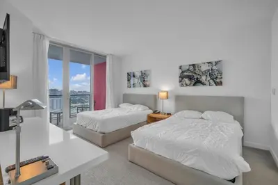 a white bedroom with two beds and a balcony at Stunning 30th-Floor Studio at Beachwalk Resort in Hallandale Beach