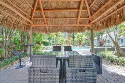 a patio with a table and chairs under a straw roof at Tropical Oasis 2BR w Pool in Fort Lauderdale