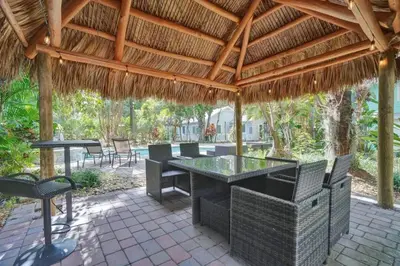 a patio with a table and chairs under a thatched roof at Tropical Oasis Studio w Pool in Fort Lauderdale