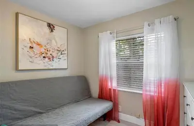 a bedroom with a couch and a window with red curtains at Sunny Cottage in Fort Lauderdale