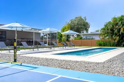 a swimming pool with chairs and umbrellas in front of a house at Pickleball fun Family home near Hard Rock Stadium in North Miami