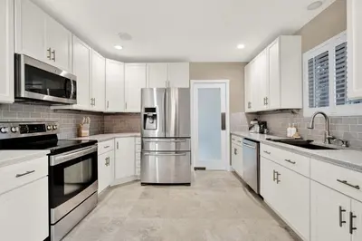 a kitchen with white cabinets and a stainless steel refrigerator at HUGE Outdoor soccer 4BR HEATED Pool house near Las Olas in Fort Lauderdale