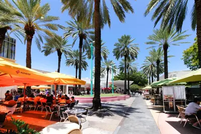people sitting at tables under umbrellas in a sidewalk with palm trees at Beachside Bliss Estate 4801 in Miami