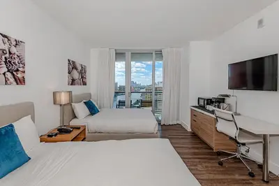 a hotel room with two beds and a desk and a television at Amazing Studio at Beachwalk on 15th Pool Gym Beach in Hallandale Beach