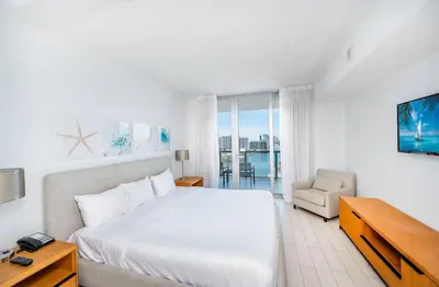 a white bedroom with a bed and a chair at Beachwalk 2 Bedrooms & Kitchen in Hallandale Beach