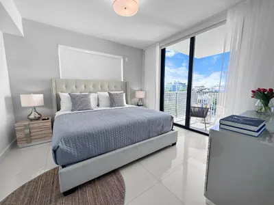 a white bedroom with a bed and a large window at Bay Breeze Premium Apartments by Eskape Collection in Miami Beach
