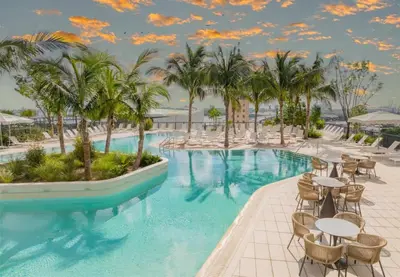 a resort pool with tables and chairs and palm trees at 1BR Apartment - Pool & Gym in Miami