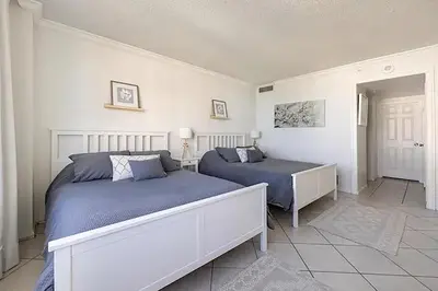 two beds in a bedroom with white walls and blue sheets at Miami apartamento sobre la playa con estacionamiento gratuito in Miami Beach