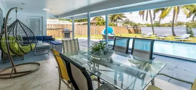 a patio with a glass table and chairs and a pool at The Miami Enchanted Lake House in Ojus