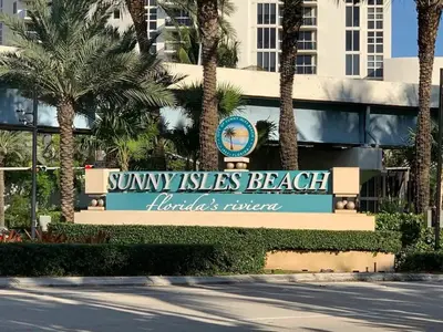 a sign in front of a building with palm trees at Apartment 2BR 2BTH - Free Parking in Sunny Isles Beach