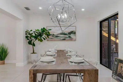 a dining room with a wooden table and a chandelier at Casa Brisa - Stylish BBQ Near heart of Kendall in Miami