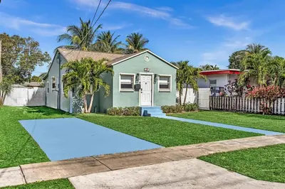 a green house with a fence and grass at Dream Hollywood Beach Retreat With Jacuzzi and Fire Pit in Dania Beach