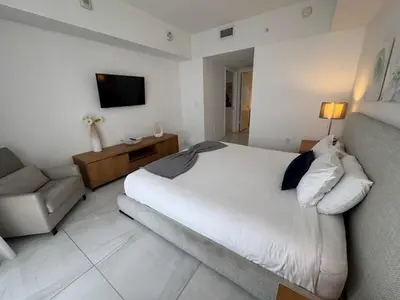 a bedroom with a bed and a couch and a television at 1BR on Miami Beach with Beach Service & Near Mall in Hallandale Beach