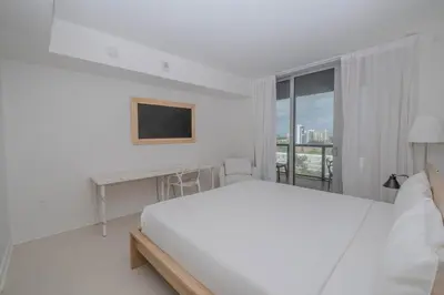 a white bedroom with a bed and a desk and a window at Amazing 2B 2B Luxury Beach Apmt in Hallandale Beach