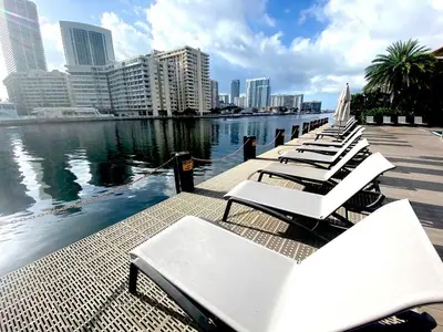 a row of white lounge chairs next to the water at Perfect getaway beach pool and gym 2B 2B in Hallandale Beach
