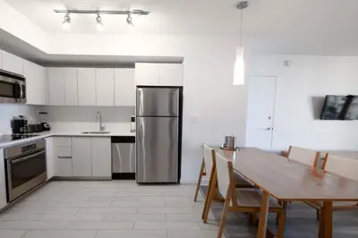a kitchen with a table and a stainless steel refrigerator at 2B 2B Beachfront Pool Gym and Restaurant in Hallandale Beach