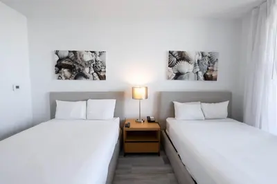 two beds in a room with a nightstand between them at 2B 2B Beachfront Pool Gym and Restaurant 2004 in Hallandale Beach