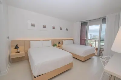 a white bedroom with two beds and a balcony at Luxury Miami Apartment Beach and Poolside drinks 2308 in Hallandale Beach