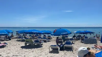 a beach with chairs and blue umbrellas and the ocean at Suite with Beach Serv Pool and close to Aventura Mall 2808 in Hallandale Beach