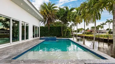 a swimming pool in front of a house with palm trees at Luxury Waterfront Home w Pool Hot Tub Dock Near Las Olas Gulfstream in Fort Lauderdale