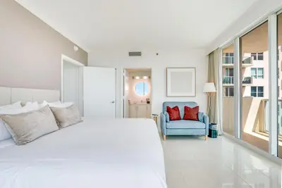 a white bedroom with a large bed and a blue chair at 2 bedroom Bay View Beauty in Coconut Grove- Parking for 2 cars included! in Miami