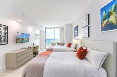 two beds in a hotel room with a desk and a bedroom at Luxury Beachfront Condo W Top Amenities in Hollywood