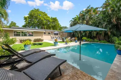 a swimming pool with chairs and an umbrella next to a house at The Jungalo Pool & Billards in Fort Lauderdale