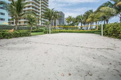 a volleyball net on a beach with palm trees and a building at Solara Surfside in Miami Beach