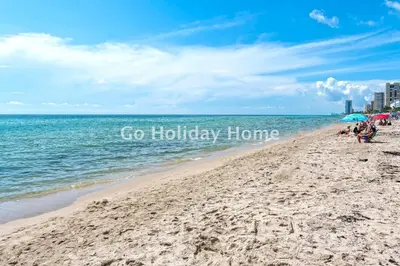 a beach with people sitting on the sand and the ocean at Hollywood Beach, 10th floor, on the beach 10T in Hollywood