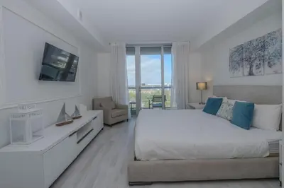 a white bedroom with a large bed and a chair at Steps from the beach 2B 2B Pool, Gym, and More in Hallandale Beach