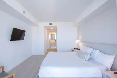 a white bedroom with a bed and a tv at Miami Apt with Amazing Views & Kitchen in Hallandale Beach