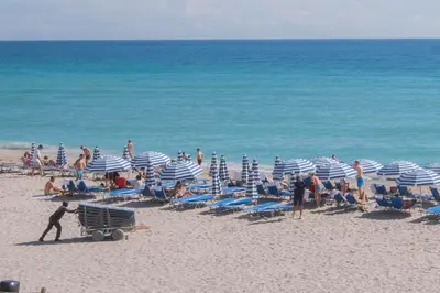 a group of people on a beach with umbrellas at Beachfront Apt with Pool by the Ocean in Hallandale Beach