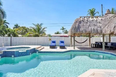 a swimming pool with two blue chairs and a straw umbrella at Blue Wave Retreat at Hollywood Beach home in Hollywood