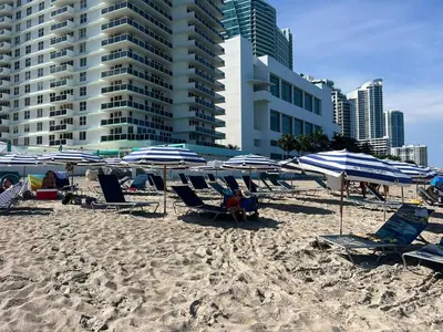 a beach with blue and white umbrellas and chairs at Studio with Service Beach and Pool Hallandale Beach in Hallandale Beach