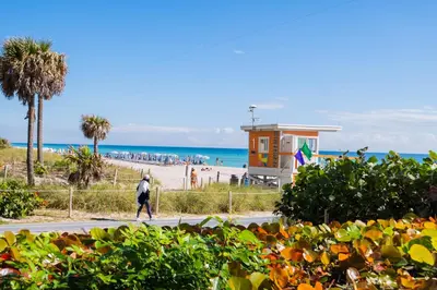 a person walking down a sidewalk near a beach at Comfy Apt 2 Queen Beds with Pool & Beach in Hallandale Beach