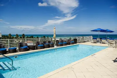 a swimming pool with chairs and an umbrella and the ocean at Beautiful 1 Bedroom with Rooftop Pool D203 in Miami Beach