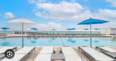a swimming pool with blue umbrellas and the ocean at Ocean front paradise studio with ocean view and beach exit in Sunny Isles Beach