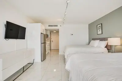 a white bedroom with two beds and a flat screen tv at Sunny Isles Beach Ocean View Studio with Balcony in Sunny Isles Beach