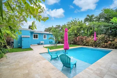 a pool with two chairs and a pink umbrella at The Frolics -Stunning Wilton Manors Pool Home in Fort Lauderdale