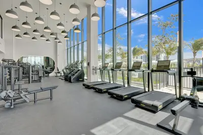 a gym with rows of tread machines and large windows at 72 Park by Nomada Residences in Miami Beach