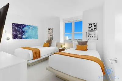 two beds in a room with white walls at Beachfront Balcony Apartment Amenities in Hollywood