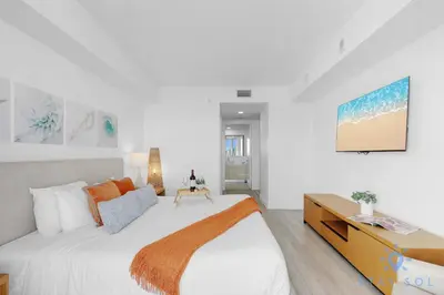 a white bedroom with a large bed and a tv at Stylish -2BR Apartment -Balcony & Pool in Hallandale Beach