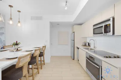 a white kitchen with a long counter and some chairs at Amazing 1BR Apt View & Balcony - Pool & Gym in Hallandale Beach