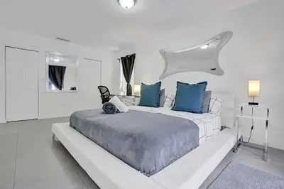 a white bedroom with a large bed with blue pillows at Central Stunning Villa with Heated Pool Cabana in Hollywood Ridge Farms