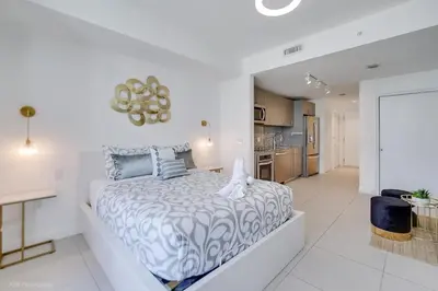 a white bedroom with a large bed and a kitchen at Stylish Studio with Pool View at the Heart of Downtown Doral in Miami