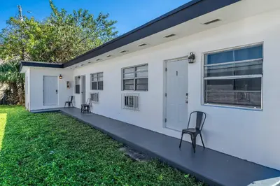 a white house with two chairs in the yard at Triplex with 3 Bedrooms, 6 Min/Beach+Free Parking in Dania Beach