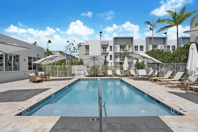 a swimming pool with chairs and umbrellas next to a building at Beachside Bliss, 1BR Condo with Pool at Dania Beach in Dania Beach