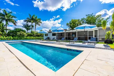 a swimming pool with umbrellas and a house at 4BR Biscayne River Home with Pool & Pickleball Fun in Biscayne Gardens